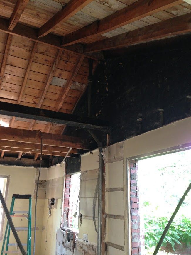 Interior of a building in demolition. Exposed rafters, charred walls, and a partially framed window.