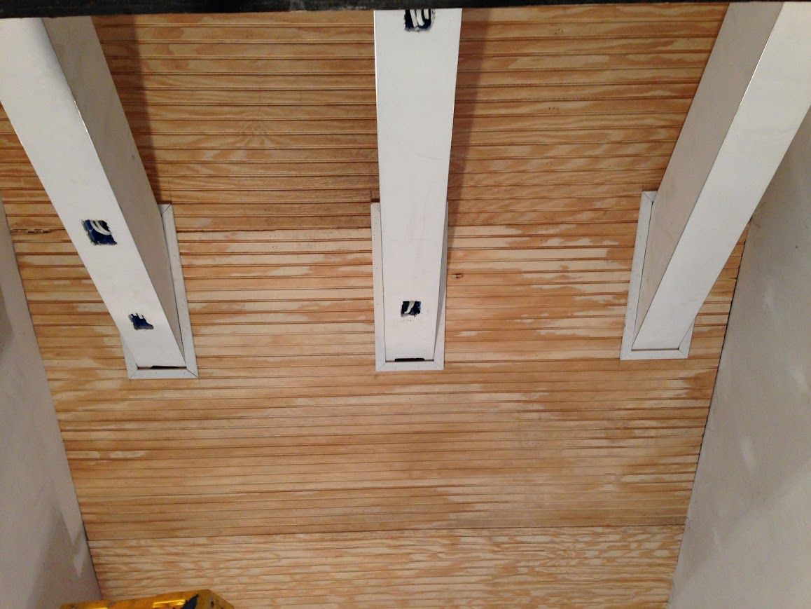 Wooden ceiling with three white support beams and brackets.