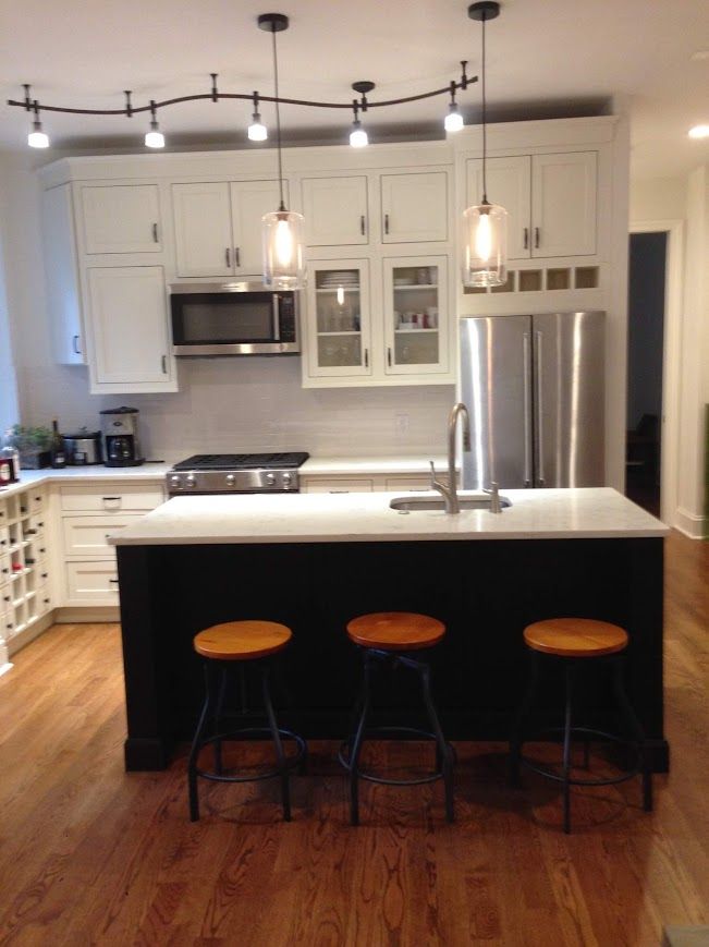 Kitchen with white cabinets, black island, stainless steel appliances, and wood floors.