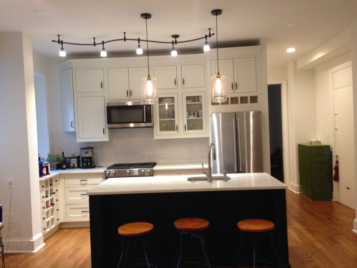 Kitchen with white cabinets, black island, track lighting, and stools.