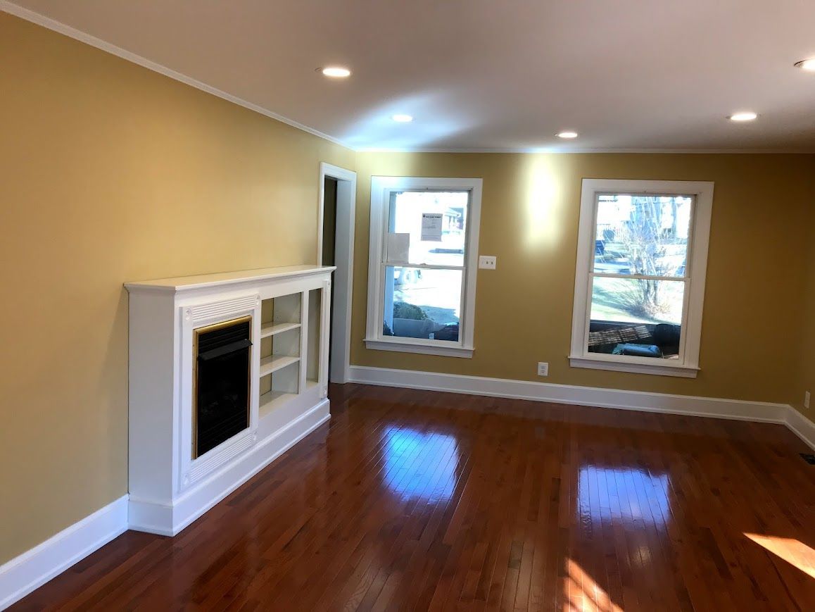 Living room with glossy hardwood floors, yellow walls, white trim, and a decorative fireplace.