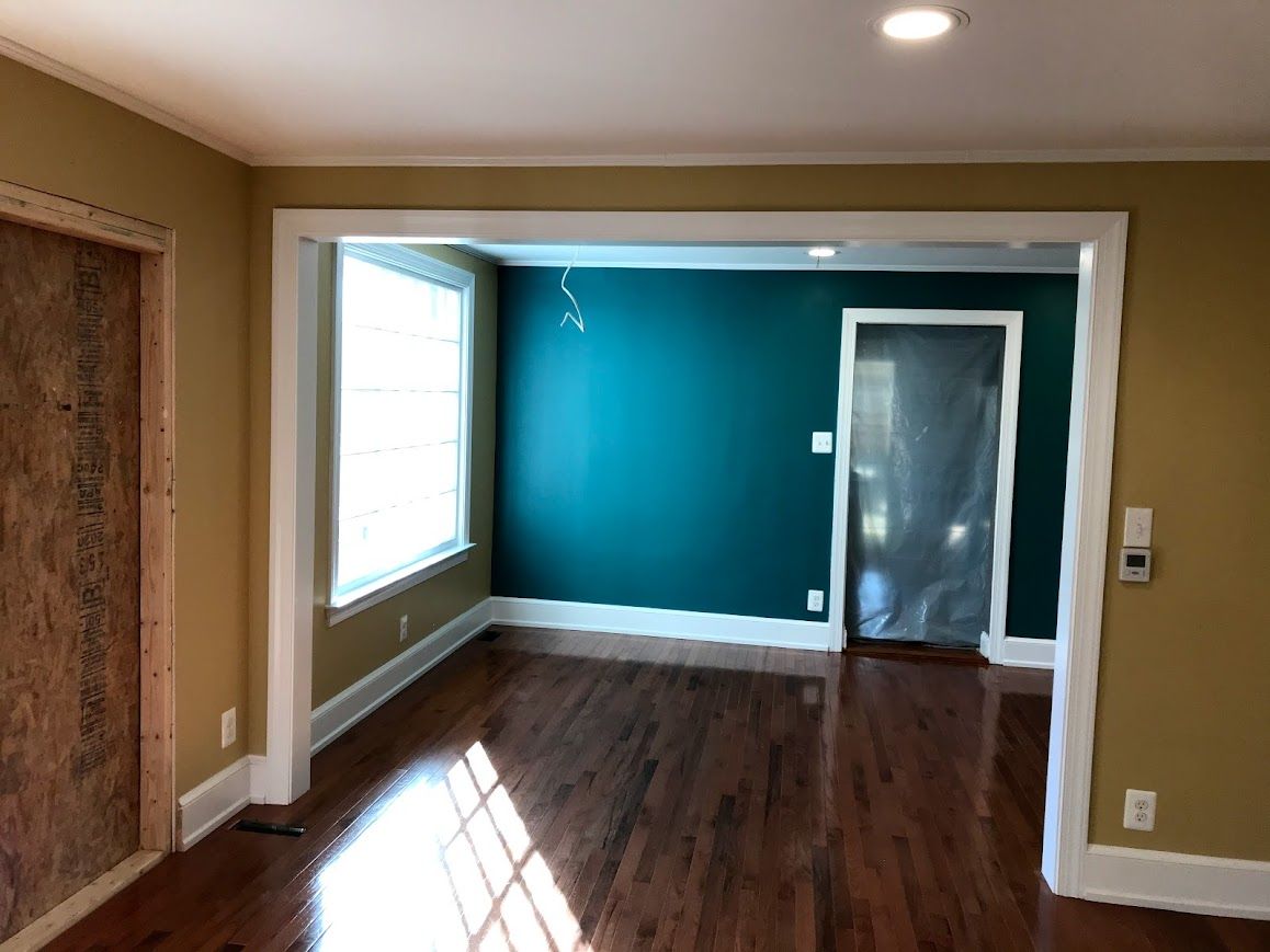 Interior of a room with a teal accent wall, white trim, and dark wood floors.