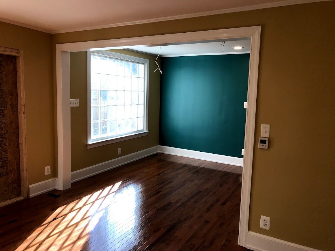 Room with wood floors, doorway to a room with dark teal wall, window.