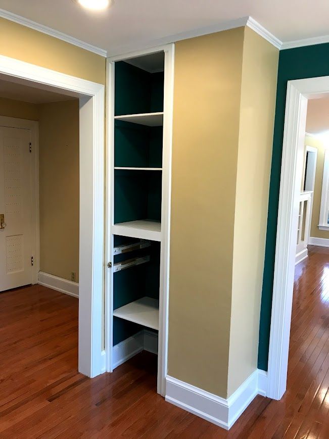 Built-in shelving unit with white shelves and teal backing, in a room with wood floors and gold walls.
