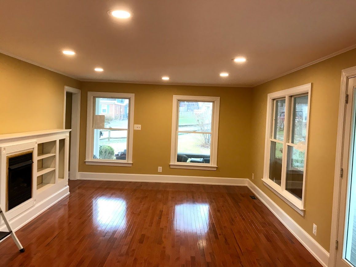 Empty living room with wood floors, yellow walls, white trim, recessed lighting, and windows.