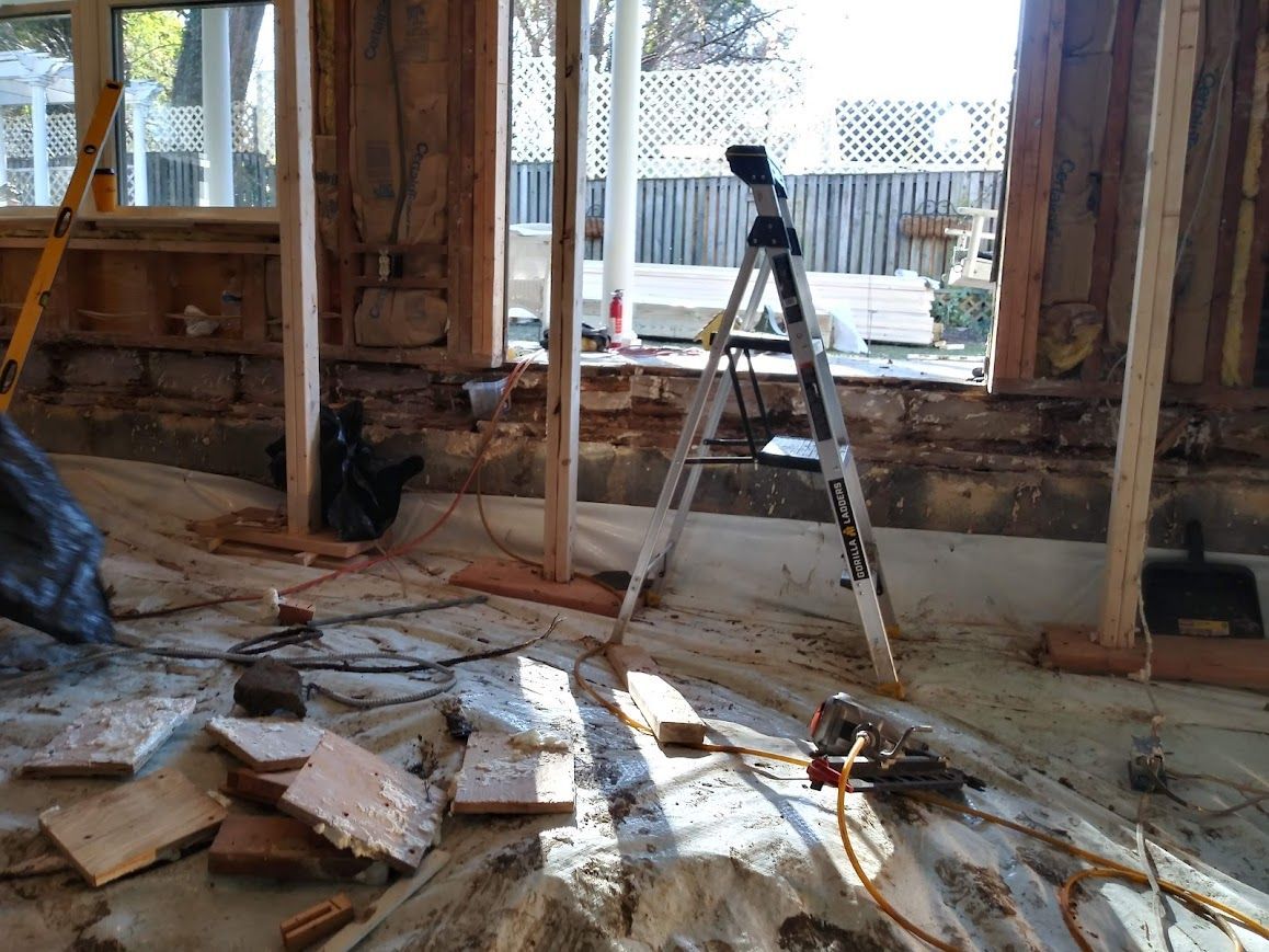 Interior of a room under construction, with exposed framing, tools, and a work light on a tripod.