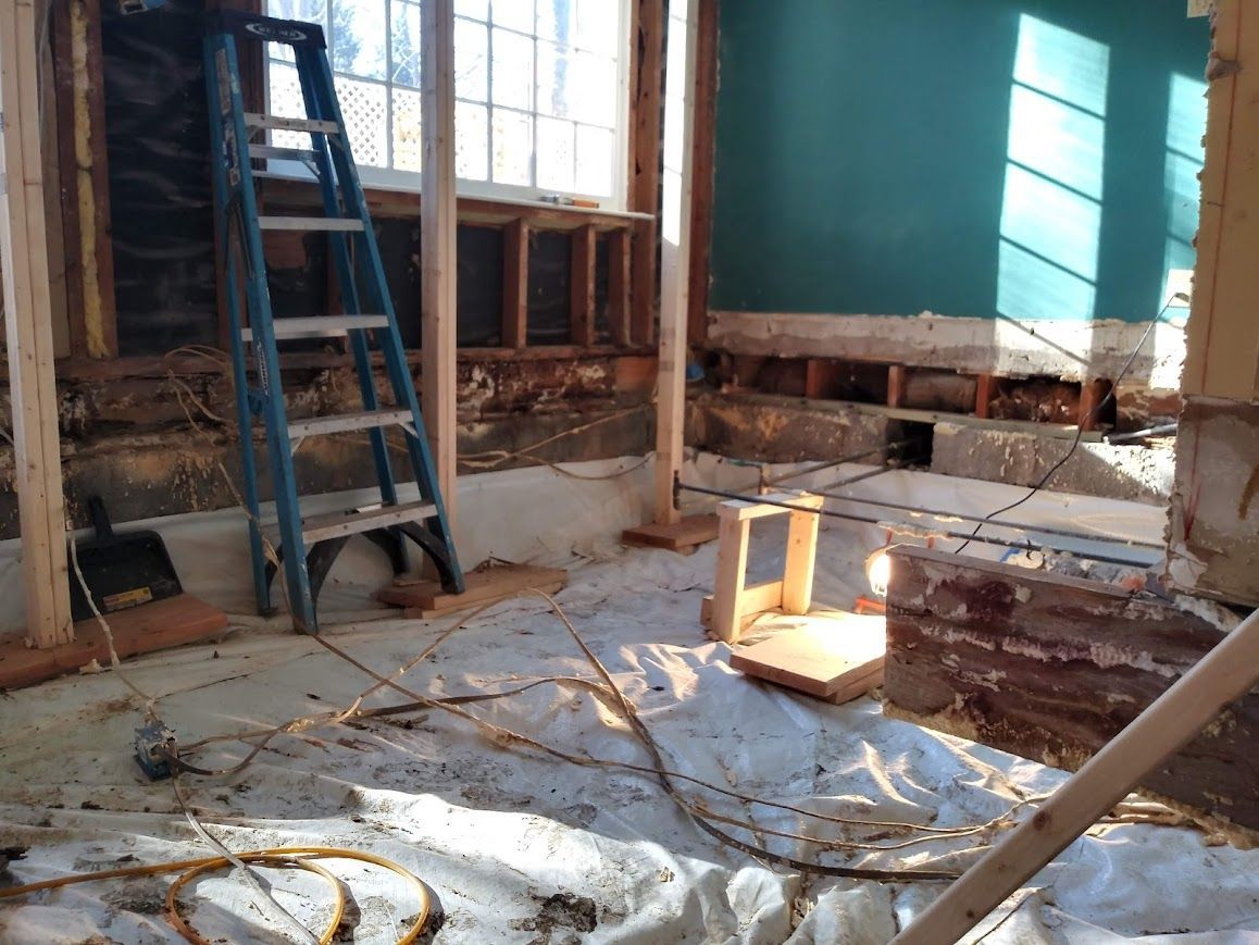 Interior room under construction with exposed walls, blue ladder, and protective sheeting.