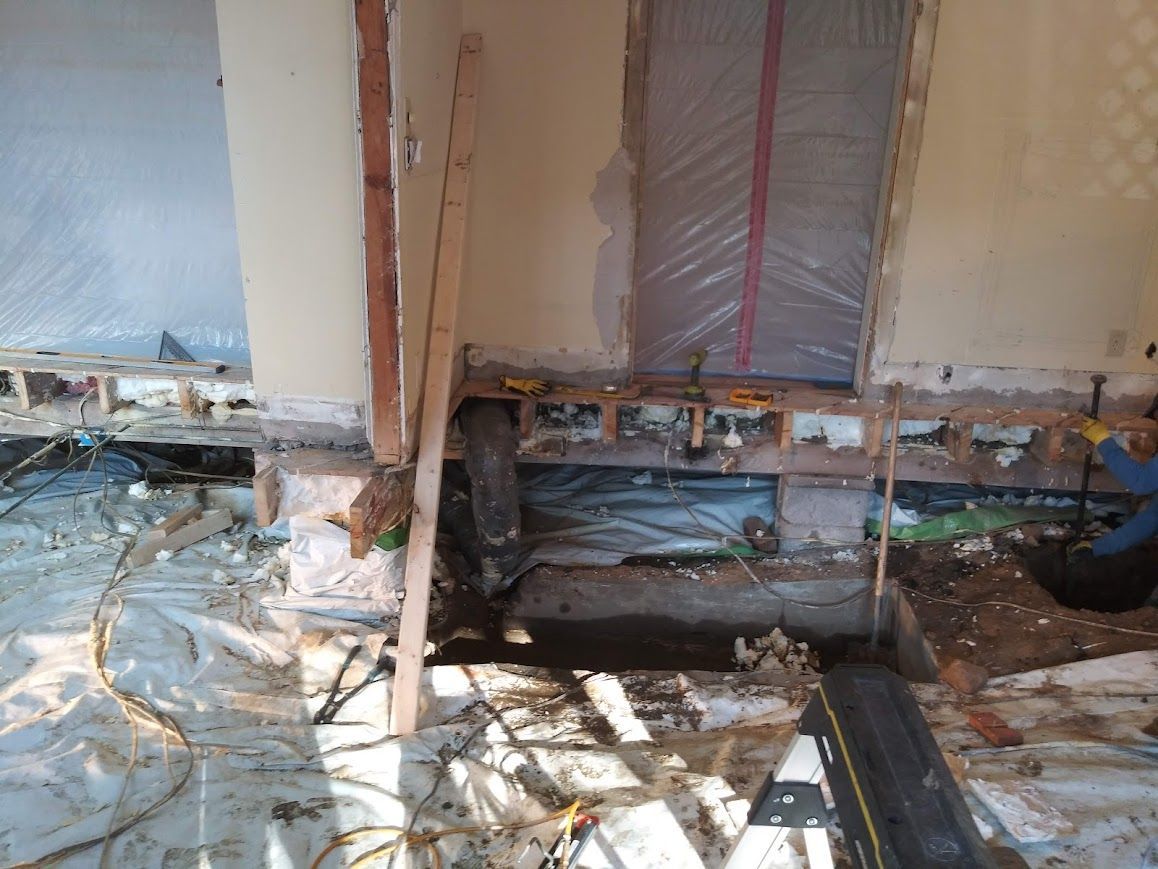 Interior view of a room under construction with exposed framing and wiring. The floor and walls are partially removed.