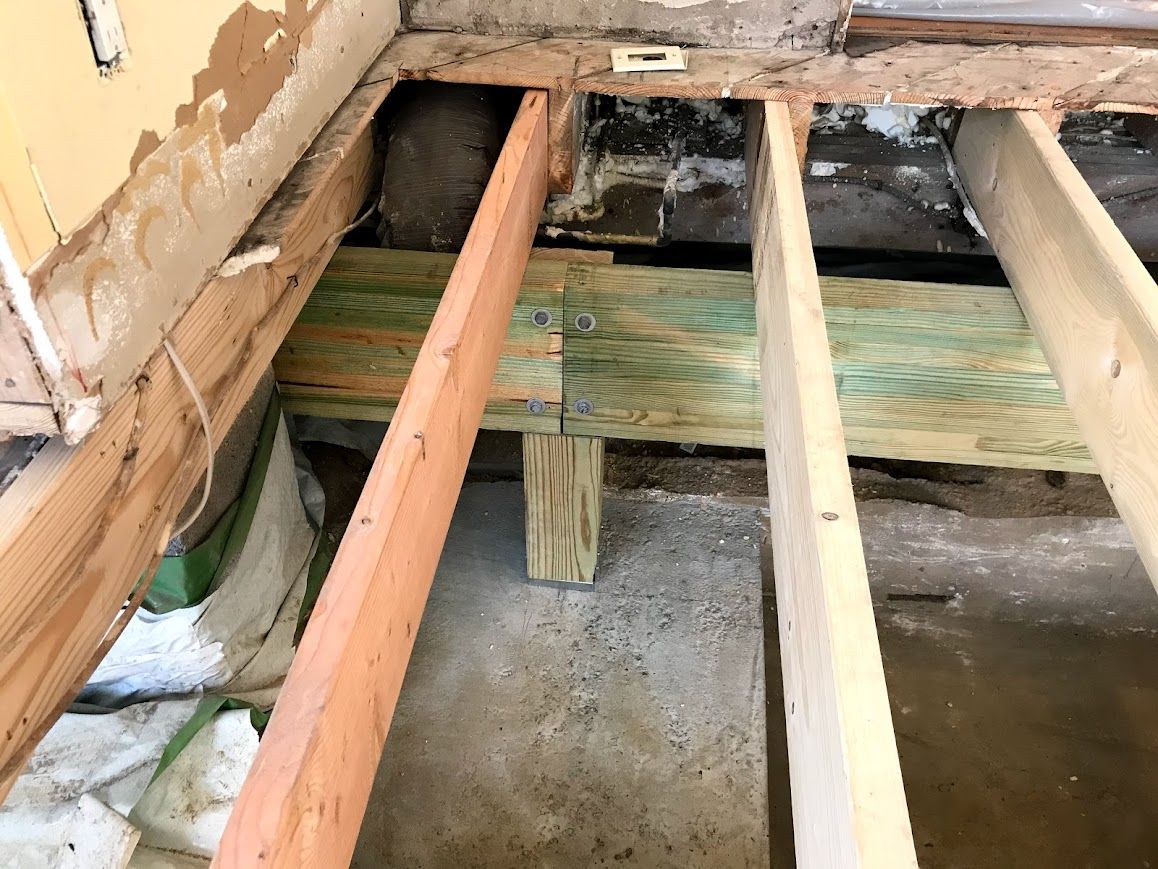 Wooden floor joists exposed in a construction site; some joists show green staining.