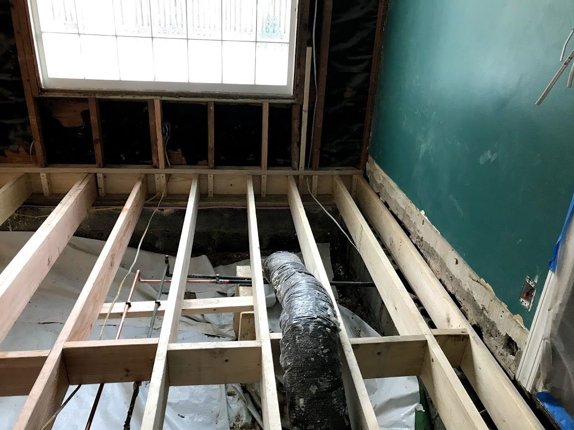 Wooden floor joists exposed in a room, with a partially open ceiling and ductwork.