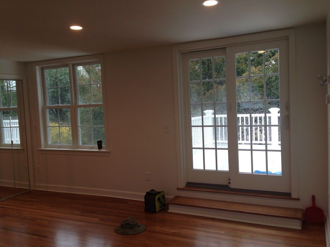 Interior room with wooden floor, white walls, windows, and a door leading outside.