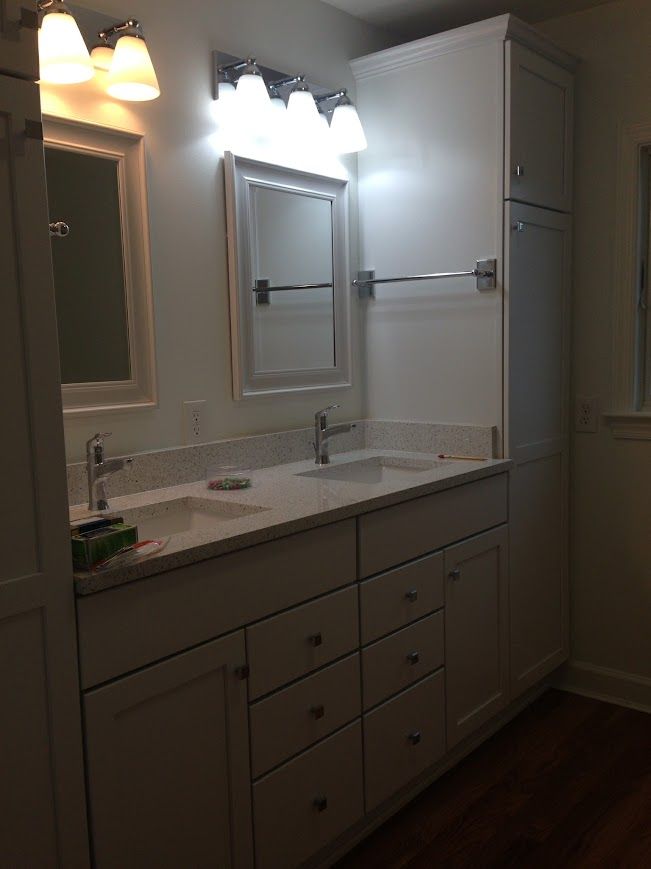 Bathroom with white cabinets, double sink, mirror, and a tall storage cabinet.