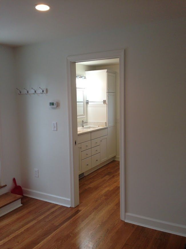 A doorway leads to a bathroom with a white vanity and cabinets. Hardwood floor in the foreground.