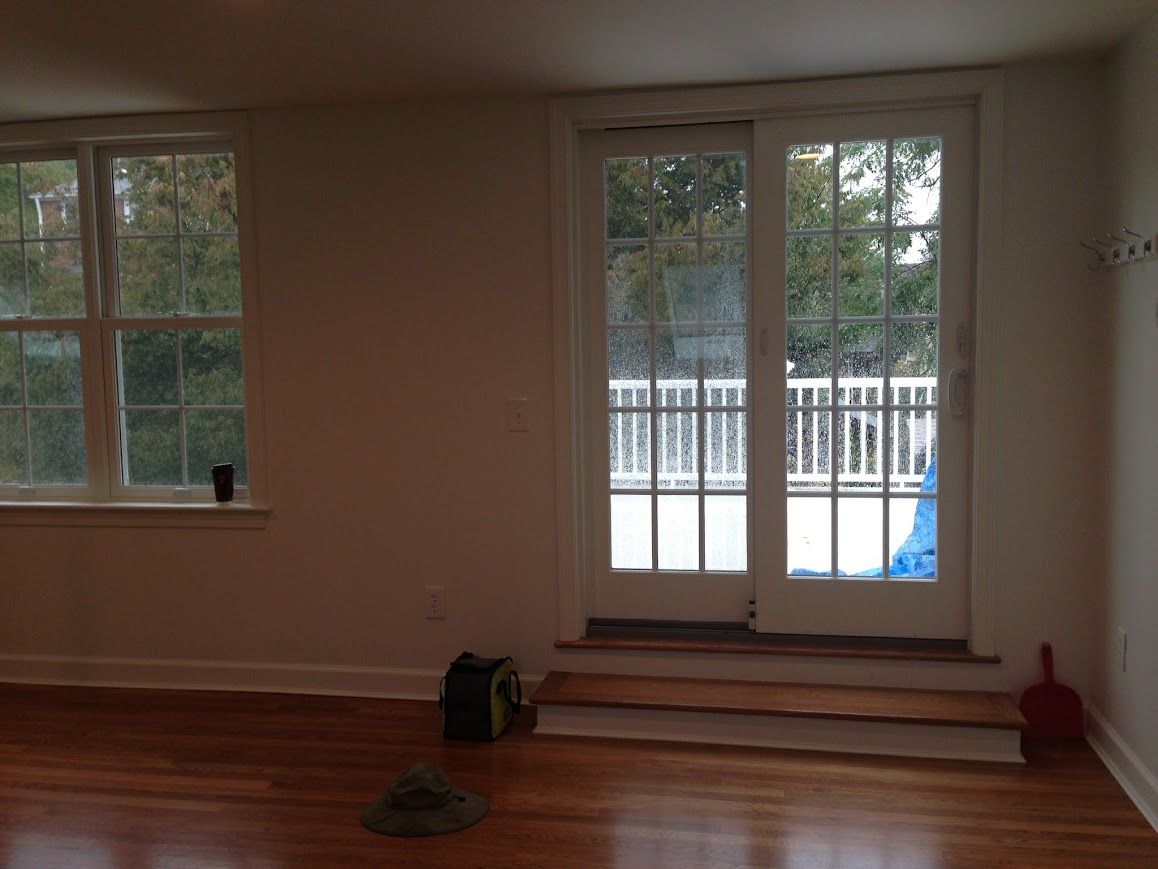 Room with hardwood floors, window and French doors leading to a balcony. A bag, hat, and brush are on the floor.