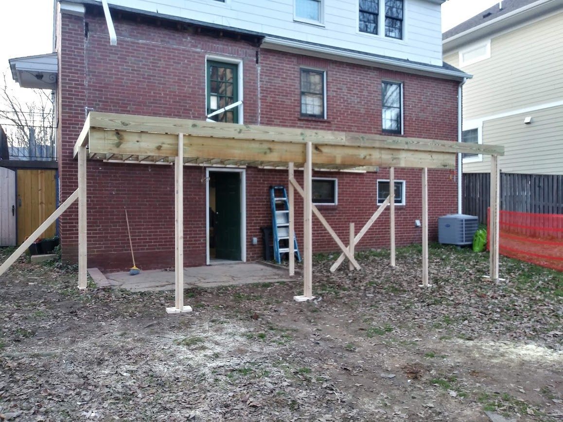 Backyard with unfinished wooden deck being constructed against a brick house.