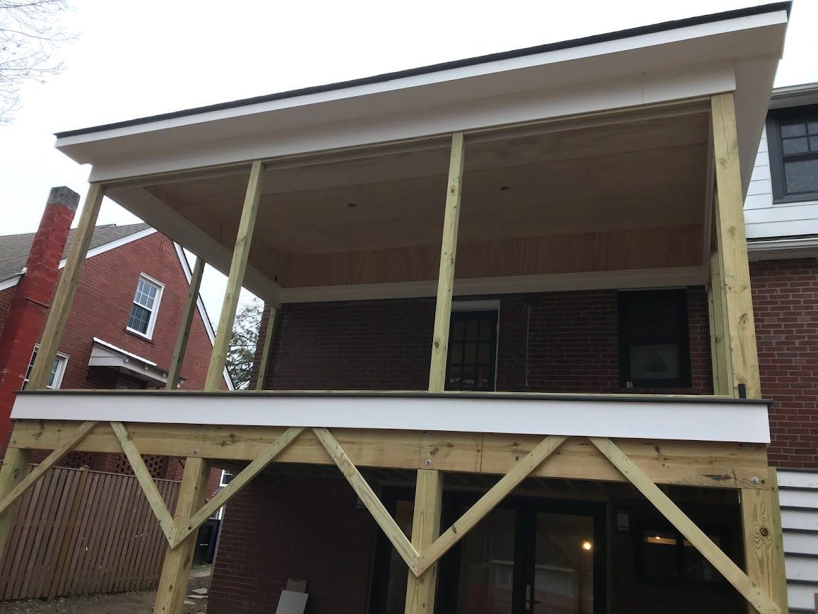 Wooden deck with an overhead roof attached to a brick building.