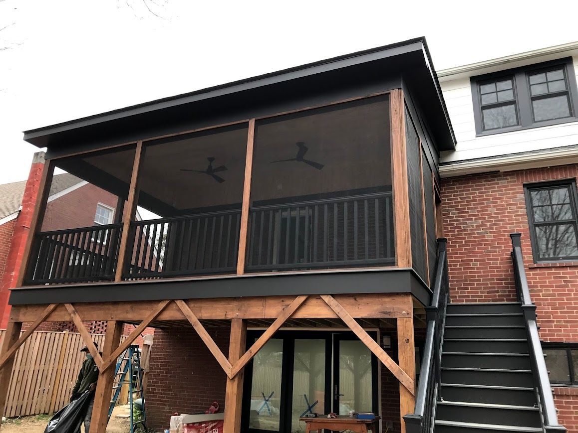 Screened-in porch addition with black trim and a dark gray roof attached to a brick building.