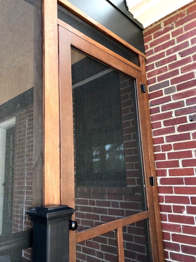 Wooden screen door on a brick building's porch.