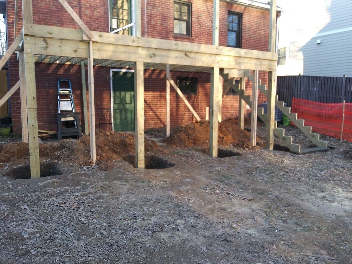 Deck construction in progress with wooden posts and a brick building background.