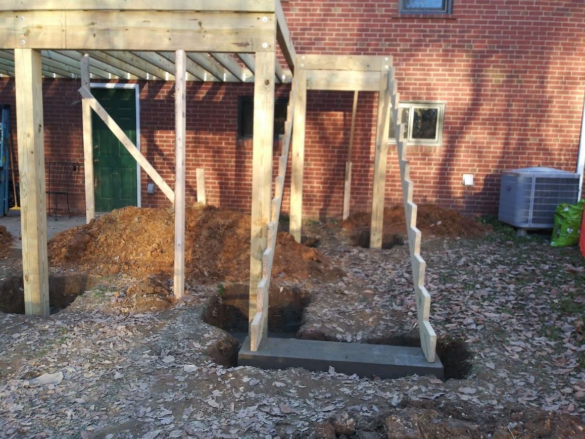 Wooden deck under construction with unfinished stairs and bare earth.