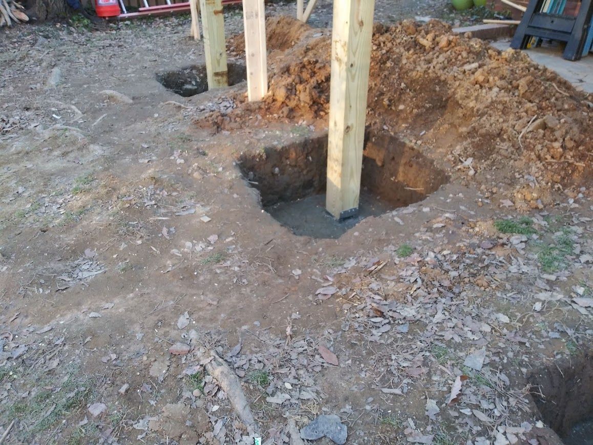 Wooden posts set in concrete foundations in dirt, likely for a structure.