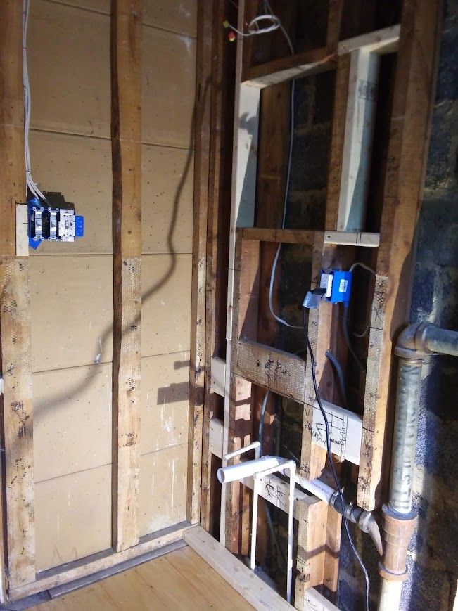 Interior wall under construction with electrical boxes and plumbing pipes.