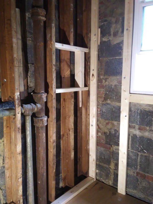 Interior view showing exposed pipes, wooden framing, and a rough brick wall.