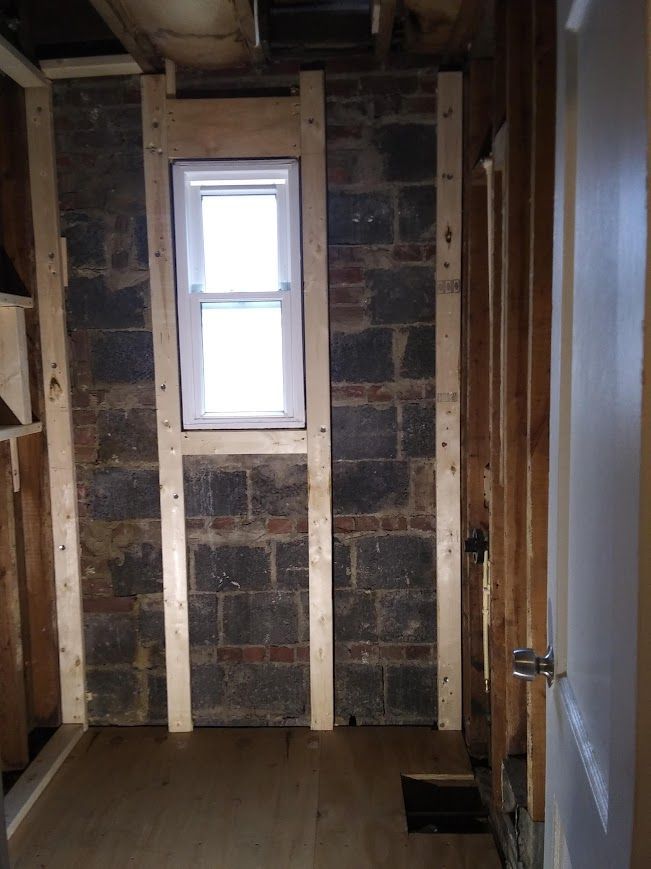 Interior wall renovation: wooden studs frame cinder block wall with window.