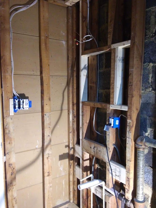 Interior wall with exposed studs, electrical boxes, wiring, and plumbing.