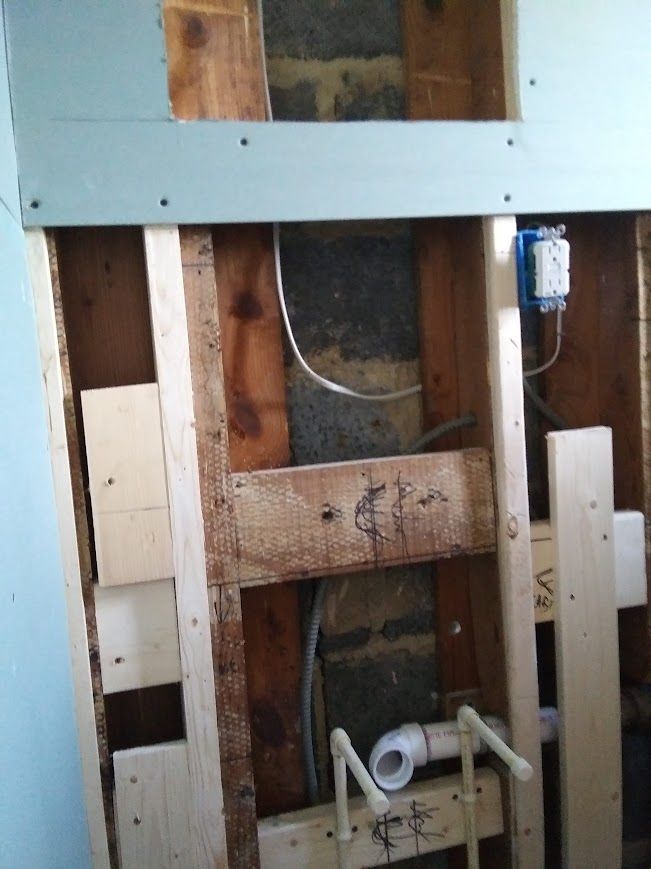Framed wall with exposed plumbing, electrical box, and wood framing.