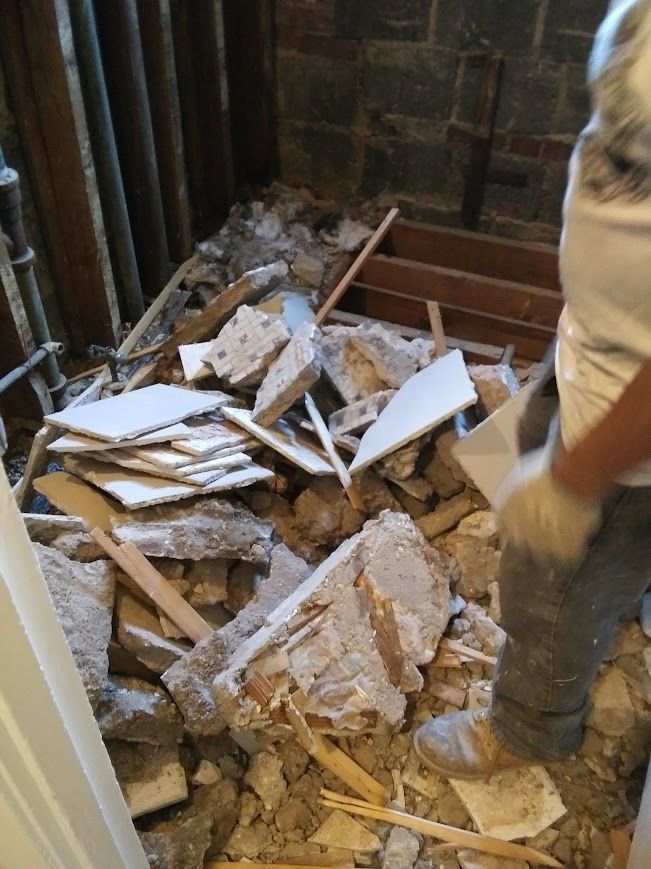 Demolition debris in a room with a person in work clothes standing.