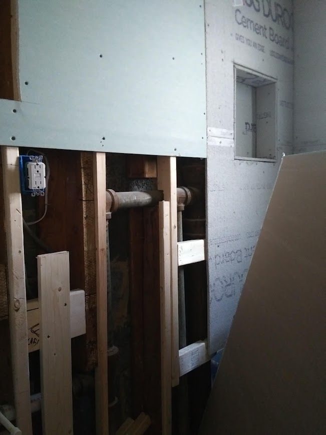 Bathroom remodel in progress with exposed pipes and partially installed cement board.