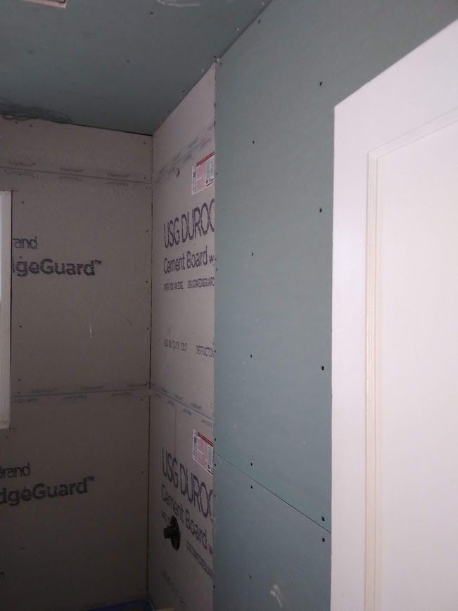 Interior bathroom wall framing; green cement board in shower, adjacent drywall, white door frame.