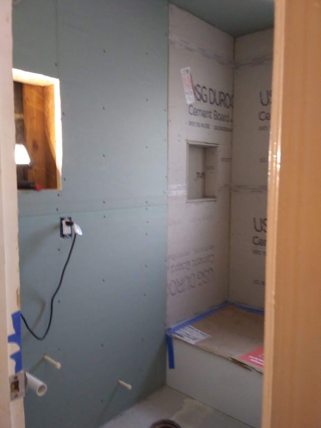 Bathroom under construction: cement board walls, shower niche, and stub-out plumbing.