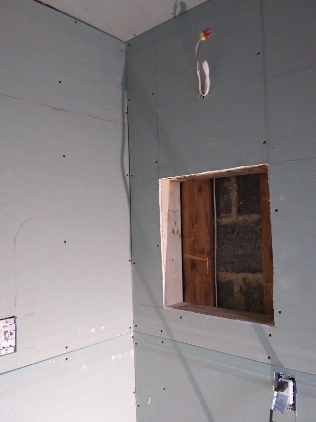 Interior construction: drywall partially installed on walls with a window opening. Electrical wiring visible.