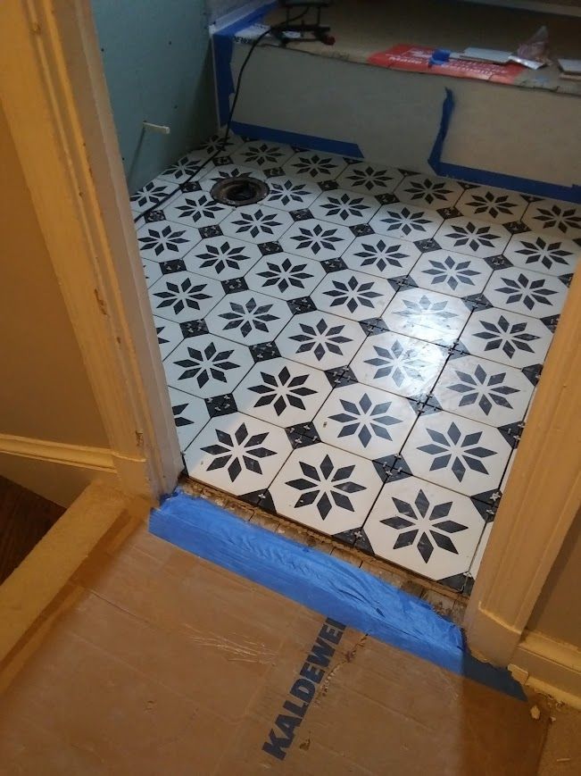 Newly tiled floor with a black and white floral pattern in a doorway, protected by blue tape.
