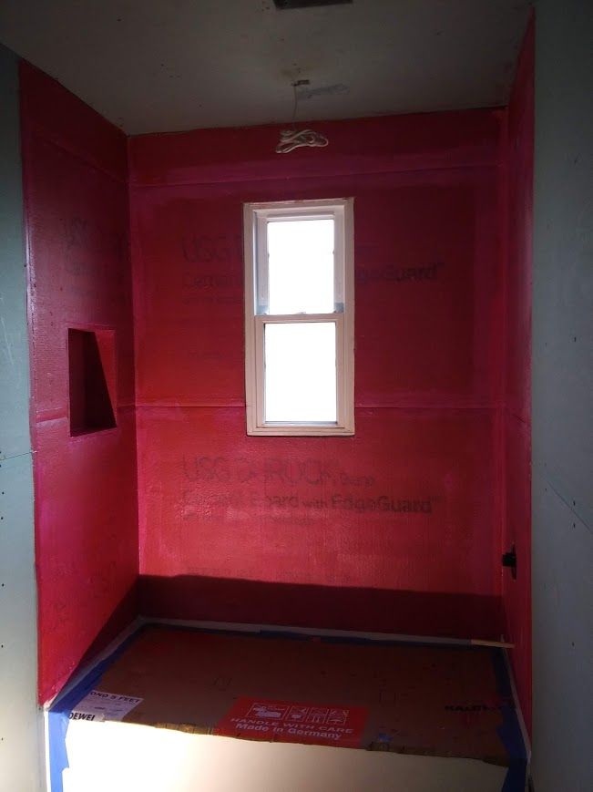 Red waterproof membrane installed in a bathroom shower, with window and recessed shelf.
