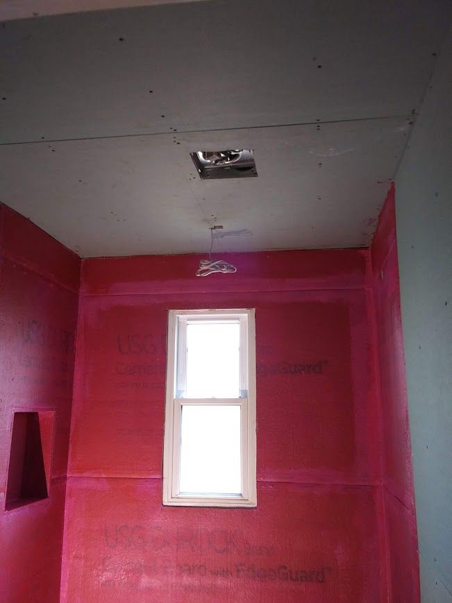 Bathroom under construction, showing red waterproof board walls, window, ceiling with electrical fixtures.