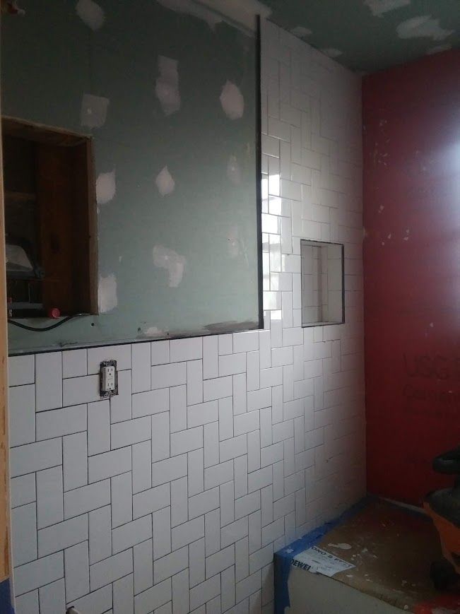 Bathroom under construction, white tiled wall with herringbone pattern, green wall, red wall, window.