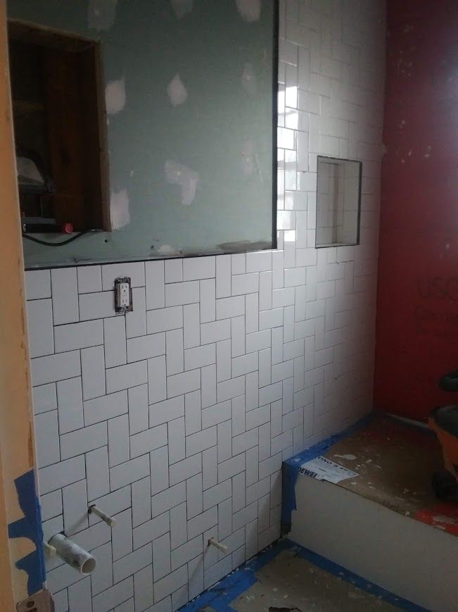 Bathroom remodel in progress; white herringbone tile on wall, unfinished surfaces, red painted wall.