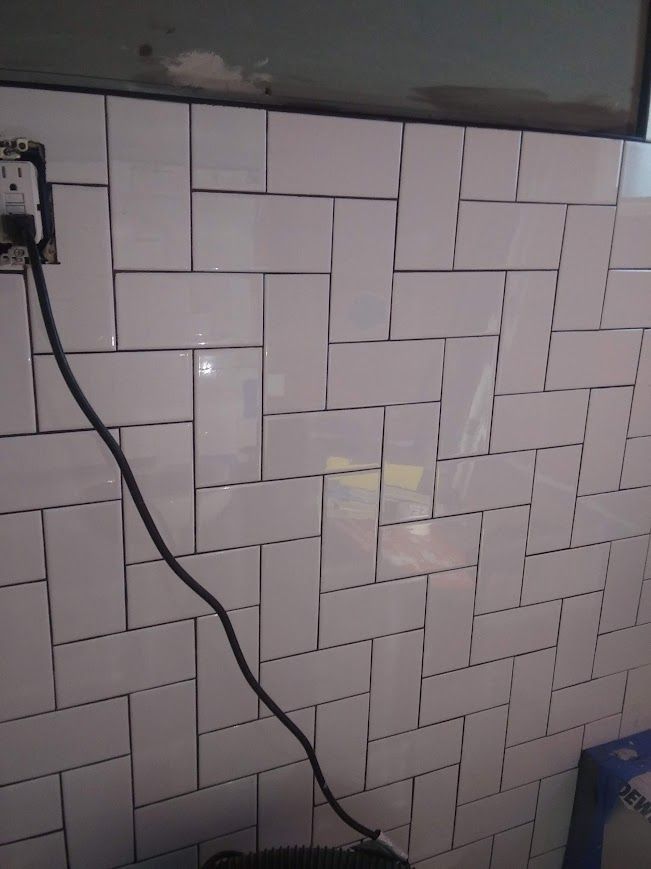 White subway tile wall with an electrical outlet and a black cord.
