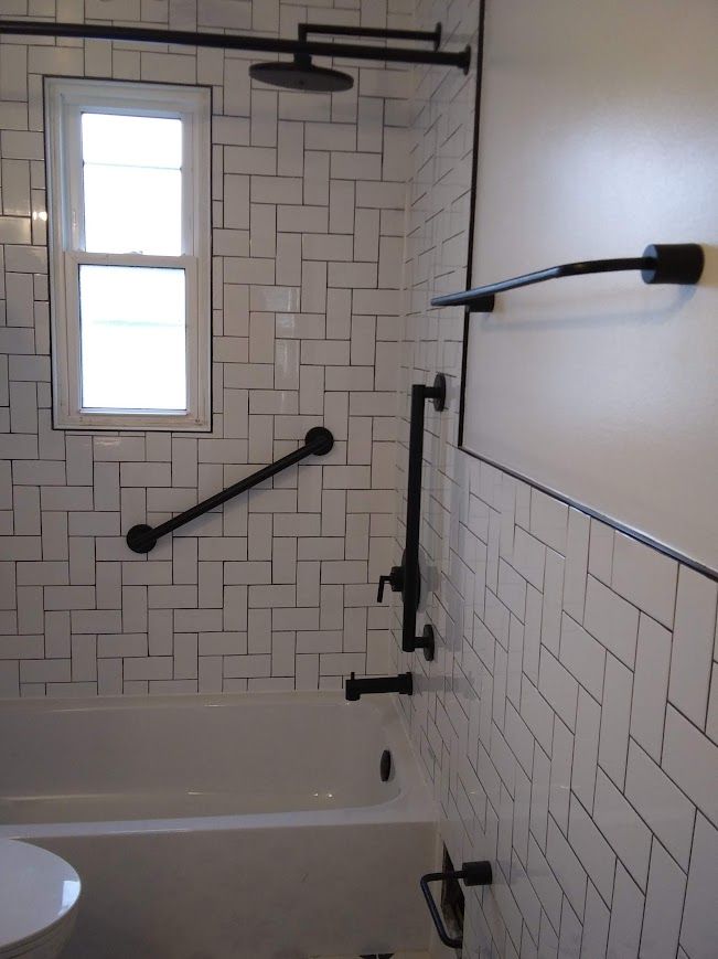 Bathroom with white subway tile in a herringbone pattern, black fixtures, and grab bars.