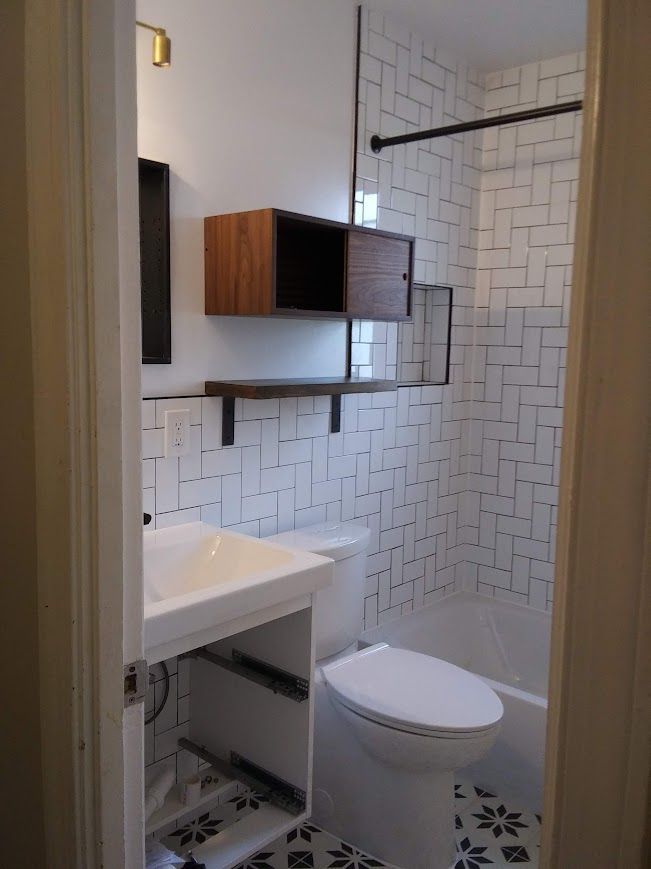 Bathroom with white subway tile, wooden cabinet, and floral tile floor.