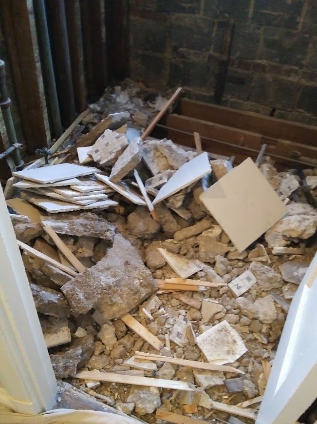 Pile of demolition debris inside a room, including broken tiles, wood, and concrete.