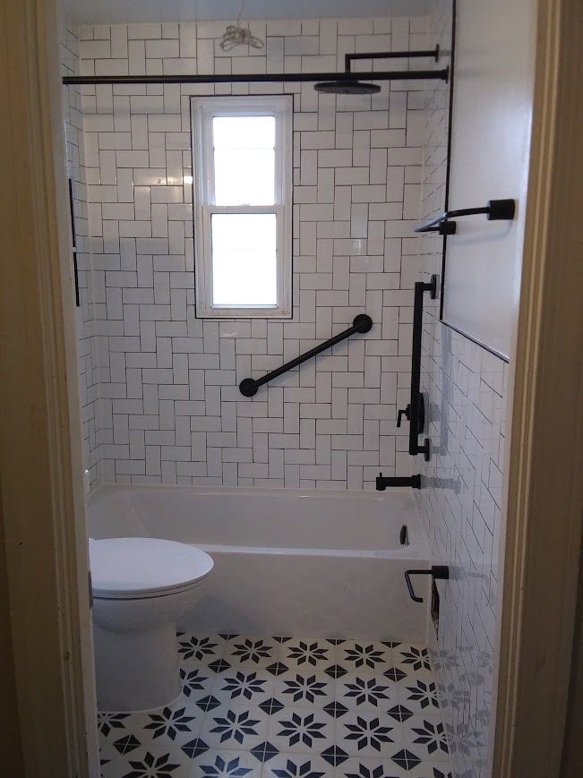 Bathroom with white and black tile, including a tub, toilet, and black fixtures. A grab bar is visible.