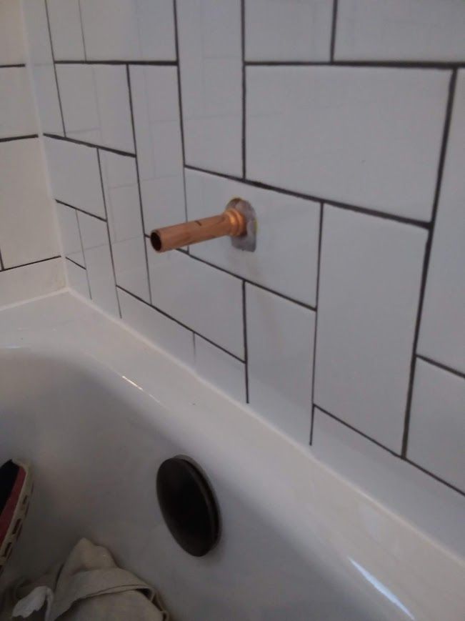 Copper pipe extending from tiled wall above a white bathtub.