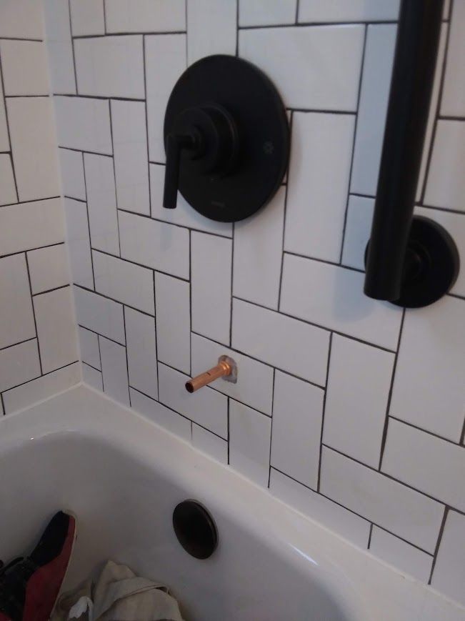 Bathroom with white tiled walls, black fixtures, copper pipe, and a bathtub.