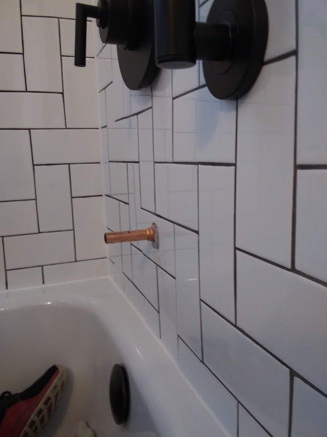 Copper bathtub spout and black shower fixtures on white subway tile.