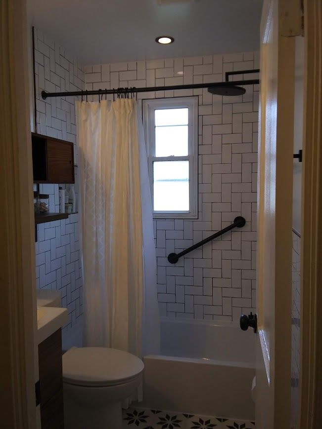 Bathroom with white tiled walls, black accents, and a grab bar.