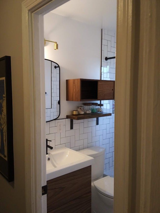 Small modern bathroom with white tile, wood vanity, and floating shelf.